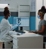 Medic holding radiography for examination with patient during coronavirus pandemic. Doctor explaining x ray scan results and diagnosis to woman, wearing face masks for protection.