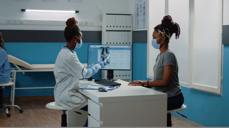 Medic holding radiography for examination with patient during coronavirus pandemic. Doctor explaining x ray scan results and diagnosis to woman, wearing face masks for protection.